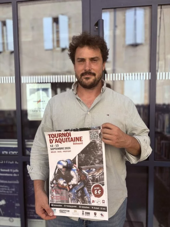 Un homme tient l'affiche du Tournoi d'Aquitaine de béhourd des 12 et 13 septembre 2026 au château Faugas, à Gabarnac.