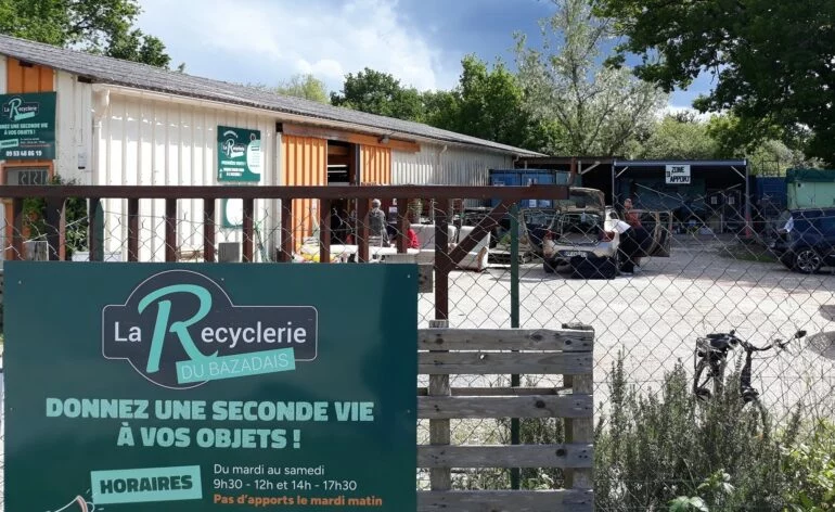 Panneau d'entrée de la Recyclerie du Bazadais avec ses horaires et le hangar de dépôt en arrière-plan