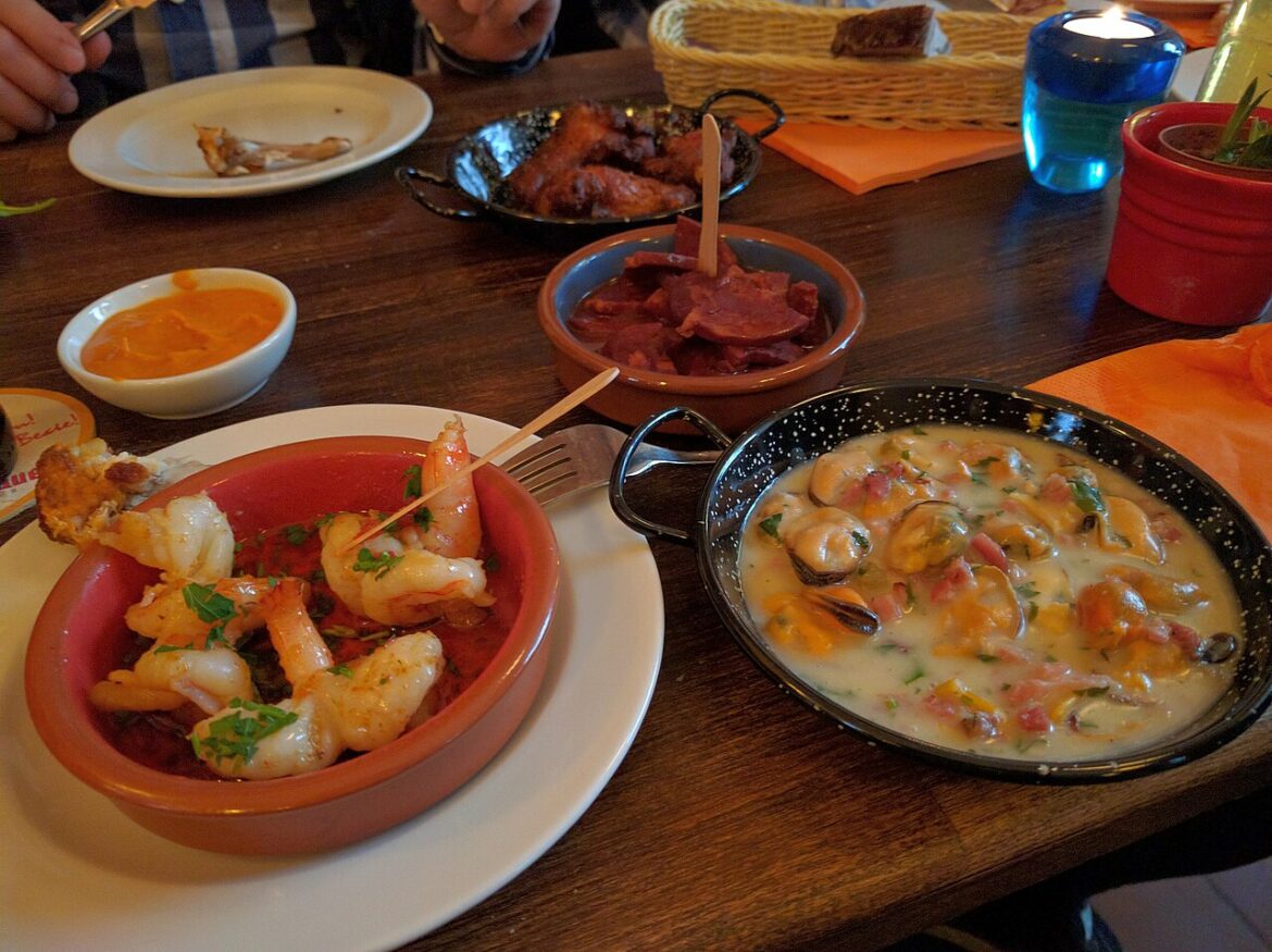 Assortiment de tapas sur une table en bois : crevettes, moules en sauce, charcuterie et sauces, pour la soirée tapas de Sainte-Gemme