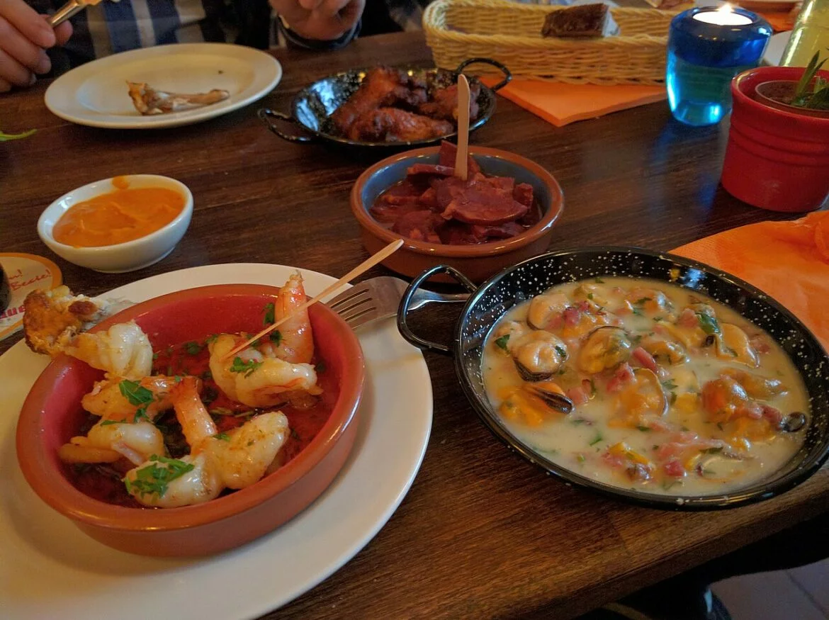 Assortiment de tapas sur une table en bois : crevettes, moules en sauce, charcuterie et sauces, pour la soirée tapas de Sainte-Gemme