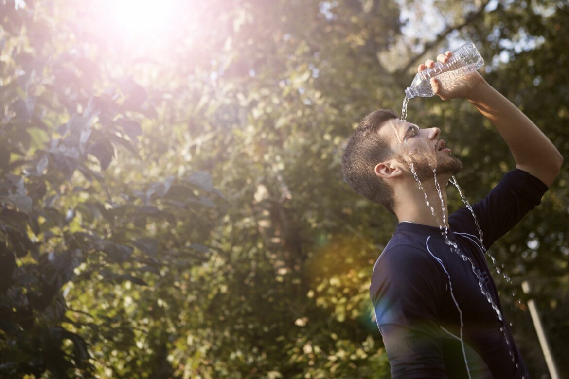 Homme qui se verse une bouteille d'eau sur le visage sous un soleil écrasant, effet de la chaleur sur le corps pendant l'été 2026