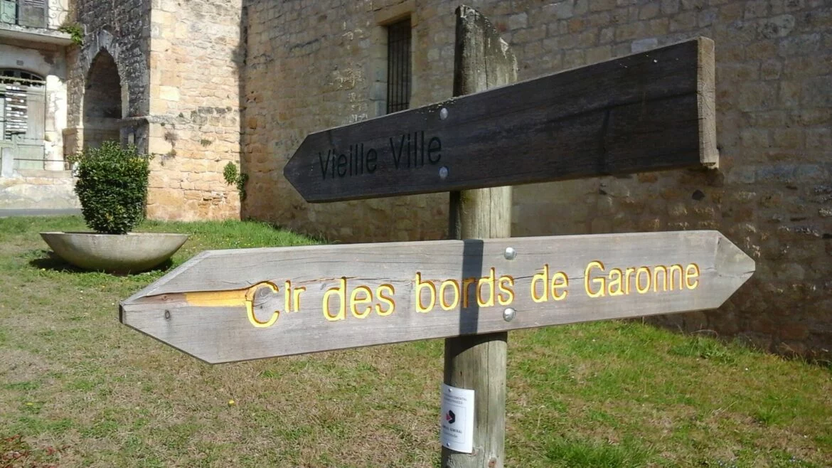 Panneau en bois du circuit des bords de Garonne devant les remparts de la vieille ville de Saint-Macaire, en Gironde